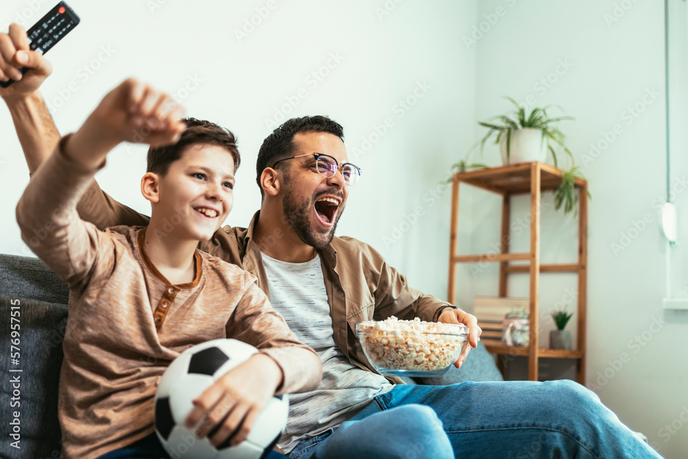 Boy watching soccer match with father at home, sitting on sofa Boy watching soccer match with father at home, sitting on sofa