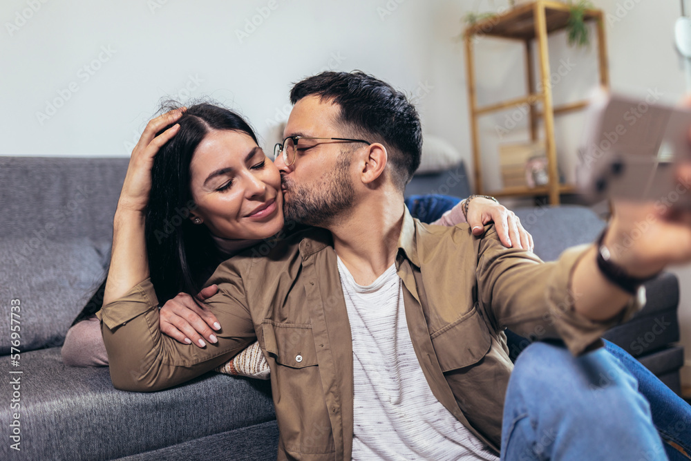 Beautiful young loving couple bonding to each other and making selfie while sitting on the couch together Beautiful young loving couple bonding to each other and making selfie while sitting on the couch together