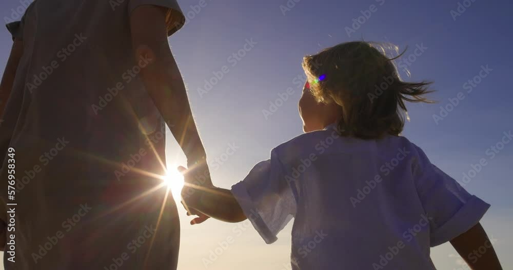 Two sisters walk outside in nature and hold hands. Younger sister runs and laughs, smiles happily and holds her older sister's hand. Siblings walk together. Love and care of older sister to younger