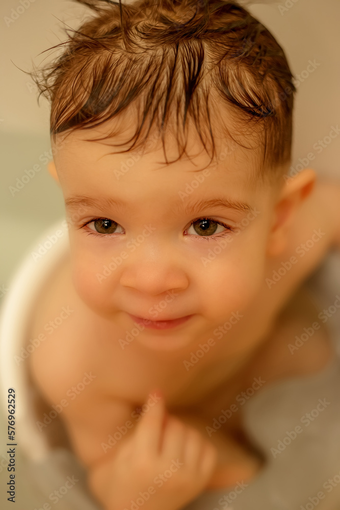 A small child sitting on a bathing chair in the bathroom A small child sitting on a bathing chair in the bathroom