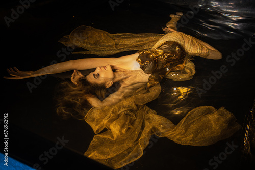 Foto Young beautiful caucasian woman in golden dress in water