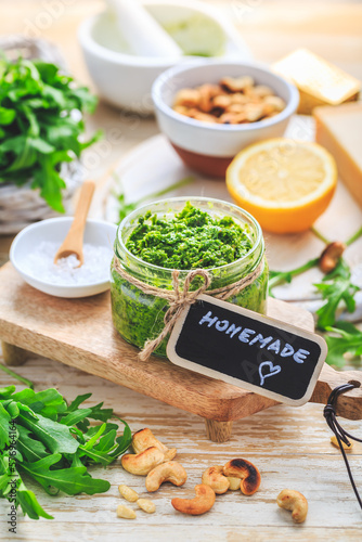 Homemade arugula pesto with ingredients on wooden background