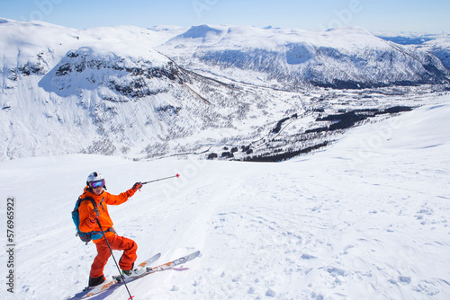 A male freerider in a red suit is standing in the snow and pointing at Myrkdalen. photo