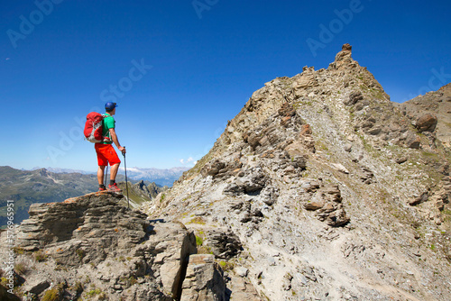 A male hiker is standing atop a rocky mountain ridge near the Forcletta pass, halfway the Haute Route.