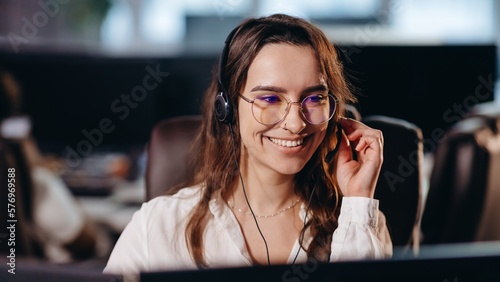 Beautiful telesales manager talking to client. Smiling hotline operator in glasses working in office. Brunette girl at her workplace in call center photo