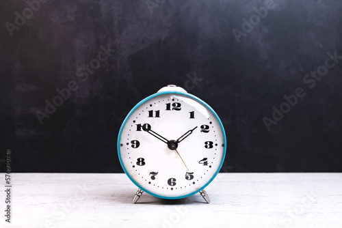 Turquoise table clock alarm clock of the era of the Soviet Union on a dark background. Show time ten minutes to two. Dial with Arabic numerals.