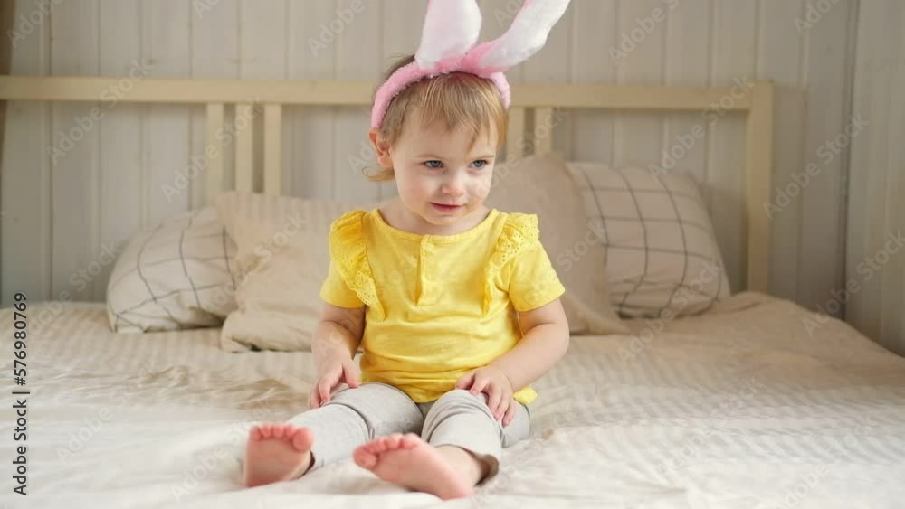 Baby girl with bunny ears. Cute funny baby play Easter eggs at home. Child playing colorful eggs indoors. Spring. Little kid celebrating Easter with traditional symbol of holiday and religion concept Baby girl with bunny ears. Cute funny baby play Easter eggs at home. Child playing colorful eggs indoors. Spring. Little kid celebrating Easter with traditional symbol of holiday and religion concept
