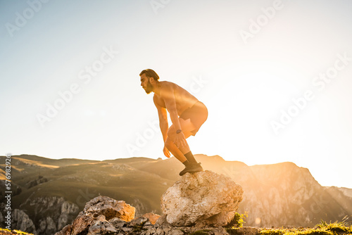Man doing conditioning training on top of a mountain in the early morning with the sunrise in the background