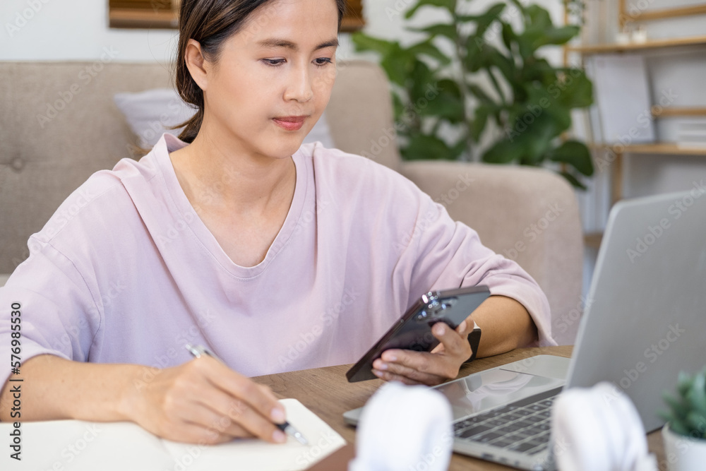 Asian woman hold phone online learning in mobile app. Girl college student using smartphone watching video course, zoom calling making notes in workbook sit in living room. Asian woman hold phone online learning in mobile app. Girl college student using smartphone watching video course, zoom calling making notes in workbook sit in living room.