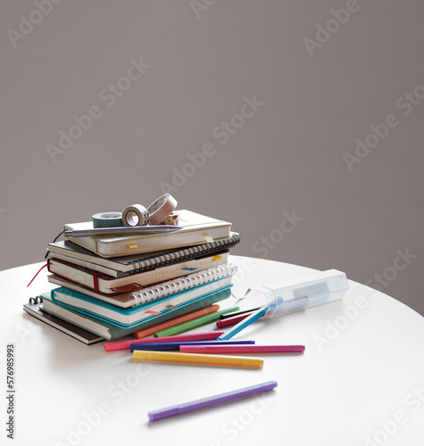 Diaries, notebooks, and colorful pens for scheduling are neatly placed on the indoor white table.