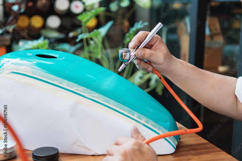 Man using airbrush tools painting color top coat on Motorcycle gas tank in garage, motorcycle maintenance and repair concept