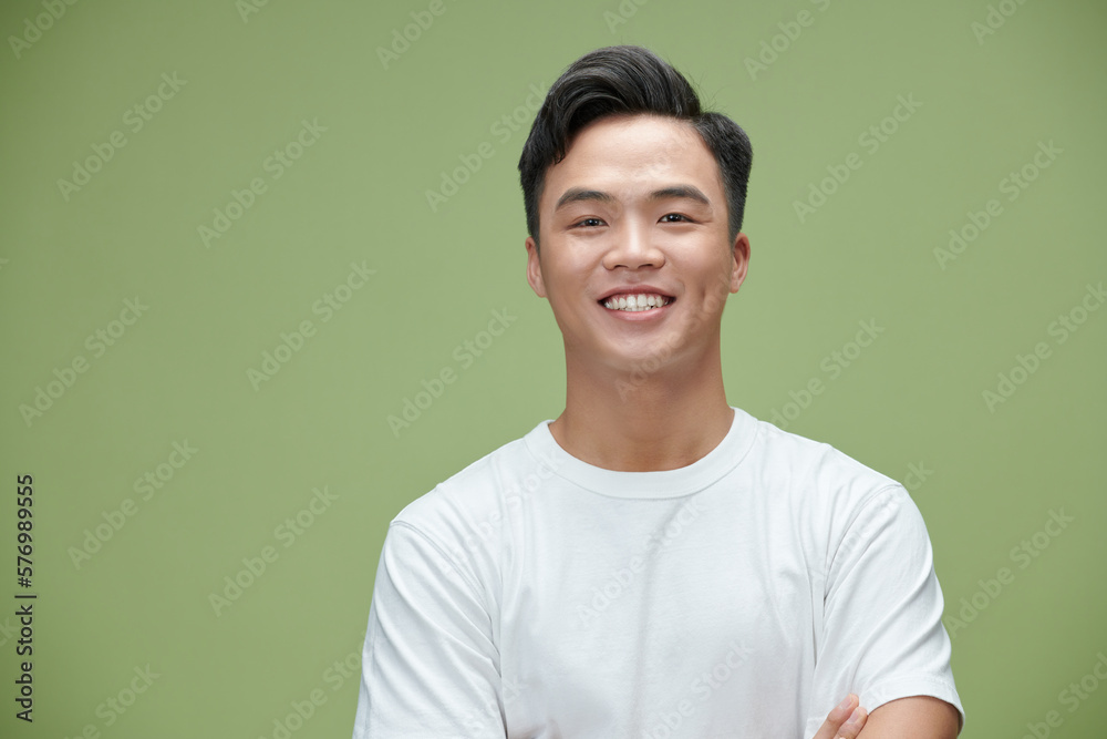 Smiling young Asian man with arms crossed in green studio isolated background Smiling young Asian man with arms crossed in green studio isolated background