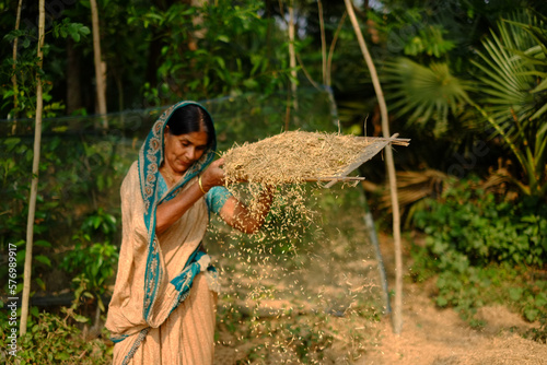 Village woman separating chaff from grain by winnowing process. South asian working woman using winnowing fan locally known as kula.  photo