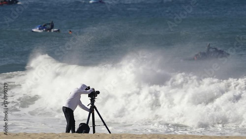 Cameraman on sandy beach shooting surfers an jetskies on big waves. Slow motion. Nazaré, Portugal. photo