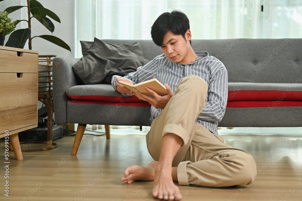 Full length of relaxed asian man sitting on floor and reading book. Leisure activity, positive mood concept Full length of relaxed asian man sitting on floor and reading book. Leisure activity, positive mood concept