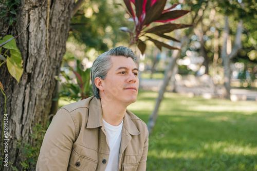 Portrait of gray-haired adult male with positive expression sitting in a park.