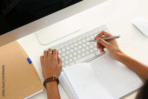 Business person writes with pen in diary on laptop keyboard in office