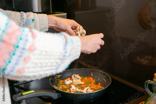 Girl cooking. Girl putting mushrooms in the pan