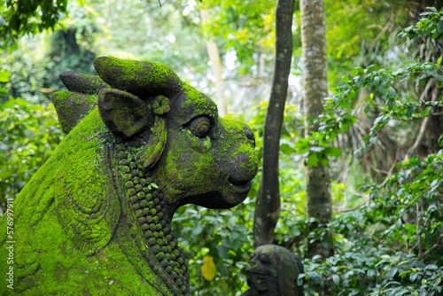 Close-up of a moss-covered mystical stone figure in the middle of a sun-drenched rainforest.