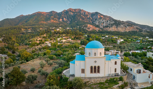 Aerial, panoramic view of the Lagoudi Zia Church on Greek island of Kos. Typical blue roofs monastery near Zia town against mountains in background. Sunset colors, no people, calm atmosphere.