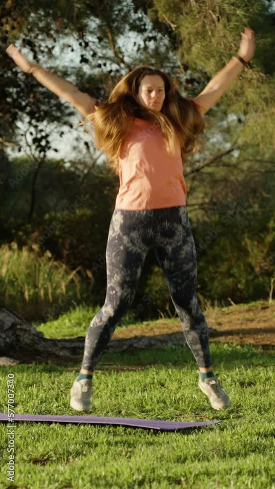 Fitness class in the forest at dawn. pine trees and green grass. Girl jumping, slow motion. Vertical video Social Media.