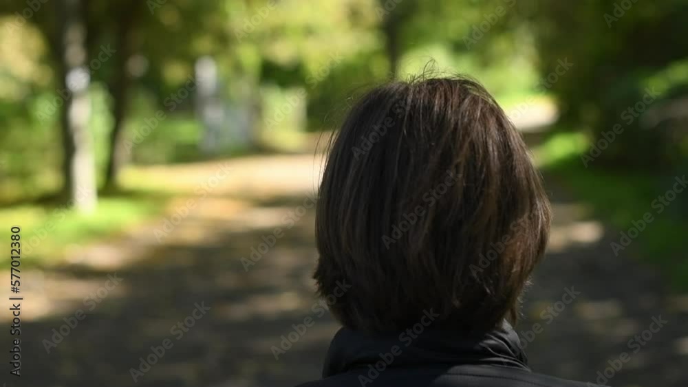 Rear view of female person walking alone in public park and looking along the road Rear view of female person walking alone in public park and looking along the road