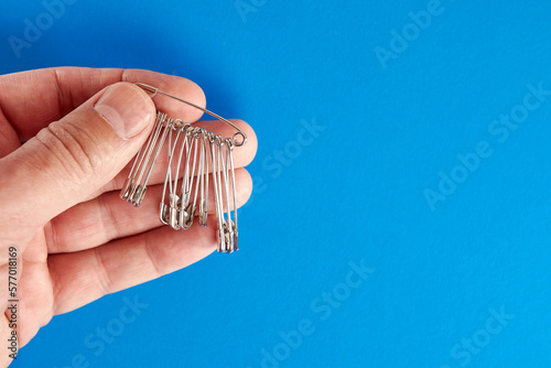 A man holds many pins in his hand on a blue background.