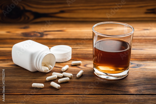 Glass with alcohol drink, whisky or brandy and drugs, white pills on wooden table. Concept of addiction and bad habits