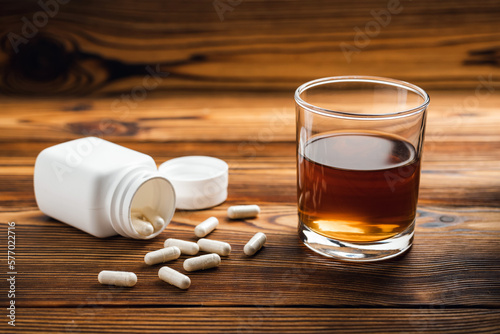 Glass with alcohol drink, whisky or brandy and drugs, white pills on wooden table. Concept of addiction and bad habits photo