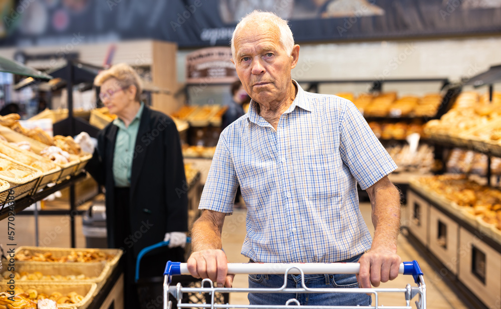 older man shopping buns and bread in bakery section of supermarket