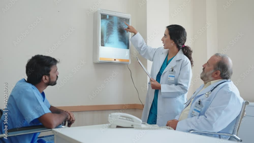 Woman medical assistant talking and explaining the X-ray results of the patient's body and there was an old male doctor sitting there listening at hospital Woman medical assistant talking and explaining the X-ray results of the patient's body and there was an old male doctor sitting there listening at hospital