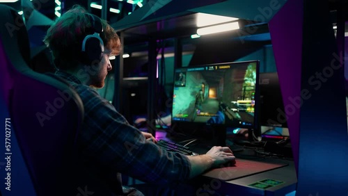 Concentrated ginger man gamer in headphones playing RPG video game on a championship. Stylish Neon Cyber Games