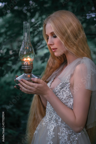 Close-up portrait of a blond girl with an oil lamp at dusk in profile