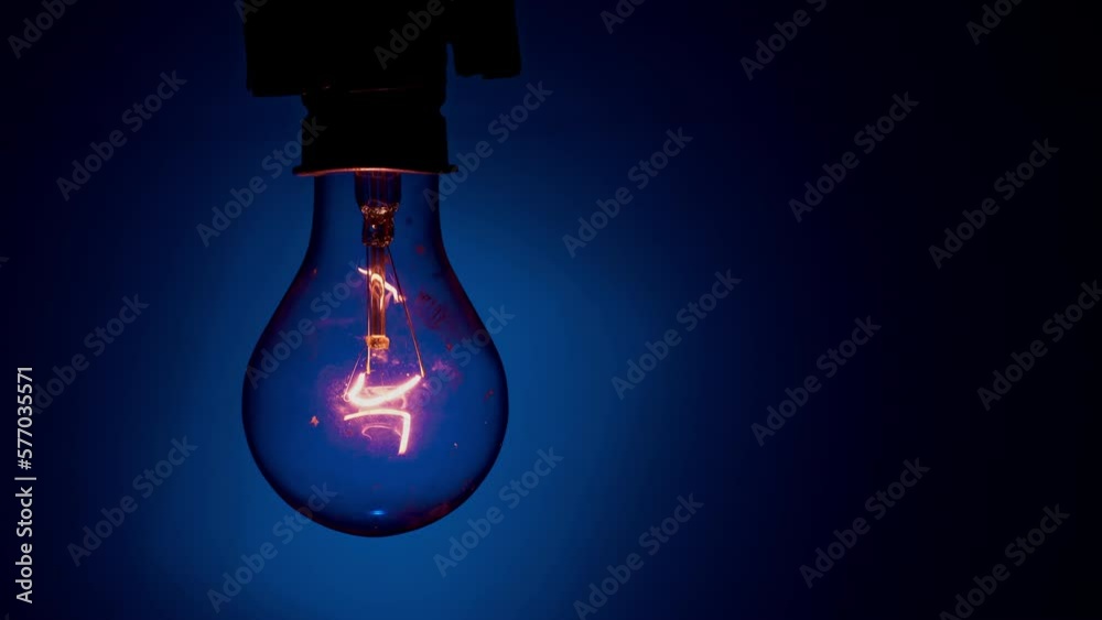 Light bulb flashes on a blue background in the dark. Slow turning on and off of a tungsten light bulb. Filament of a blinking vintage light bulb. Energy, electricity, light, life.