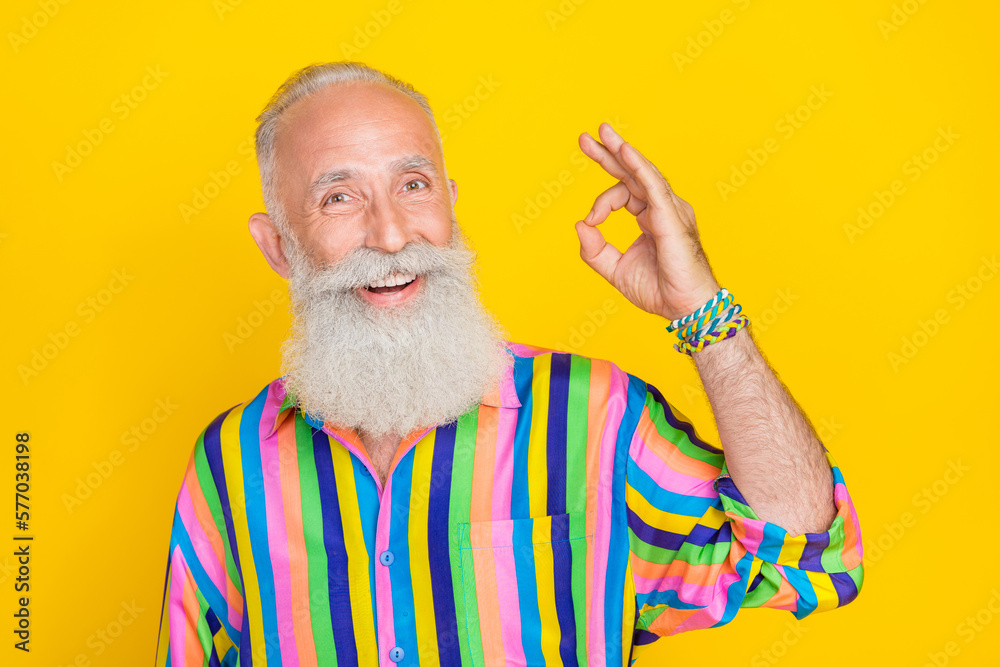 Photo of cheerful optimistic satisfied man with white beard dressed striped shirt showing okey isolated on yellow color background Photo of cheerful optimistic satisfied man with white beard dressed striped shirt showing okey isolated on yellow color background