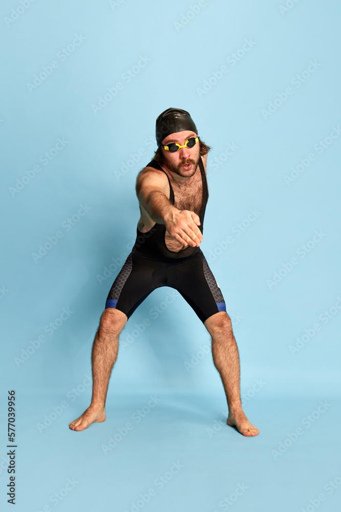Comic portrait of funny bearded man in swimsuit and swimming cap and goggles having fun isolated over blue background. Concept of sport, active lifestyle and humor Comic portrait of funny bearded man in swimsuit and swimming cap and goggles having fun isolated over blue background. Concept of sport, active lifestyle and humor