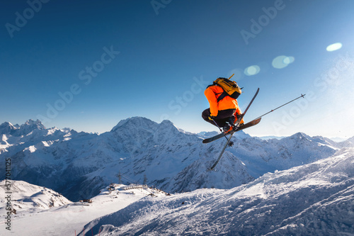 The skier jumps on the background of the blue sky and snow-capped mountains. freestyle skier performs helicopter with crossed skis simultaneously with full rotation