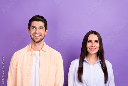 Photo of two positive minded people beaming smile look up empty space isolated on violet color background