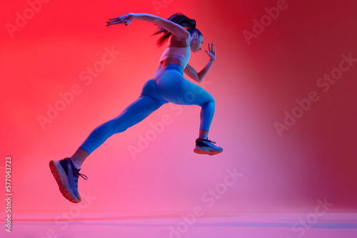 Bottom view. Young girl, professional runner athlete in uniform training, running over pink studio background in neon light. Concept of sportive lifestyle, health, endurance, action and motion. Ad photo