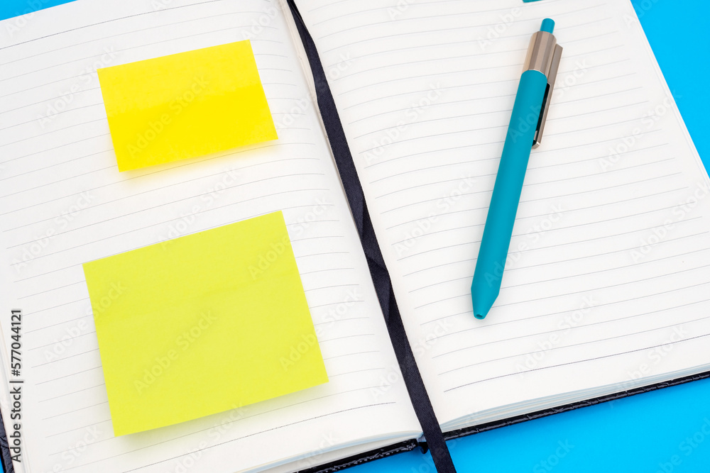 Open diary, pen and yellow reminder stickers as a concept of planning the day, organizing time, time management Open diary, pen and yellow reminder stickers as a concept of planning the day, organizing time, time management