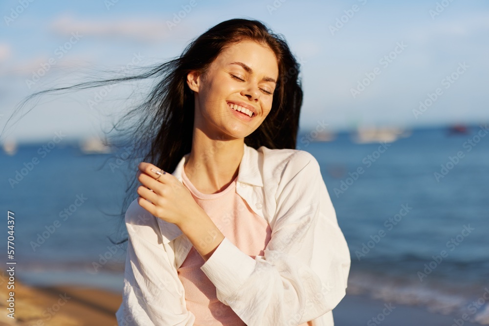 A woman with her eyes closed in the sun on a horse on the ocean smile, flying hair, tanned skin, rest, the concept of skin care in summer and spring.