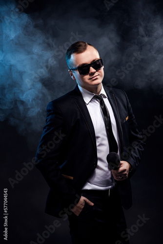 Stylish man holding microphone on dark background with smoke, actor, singer, show, host of the event
