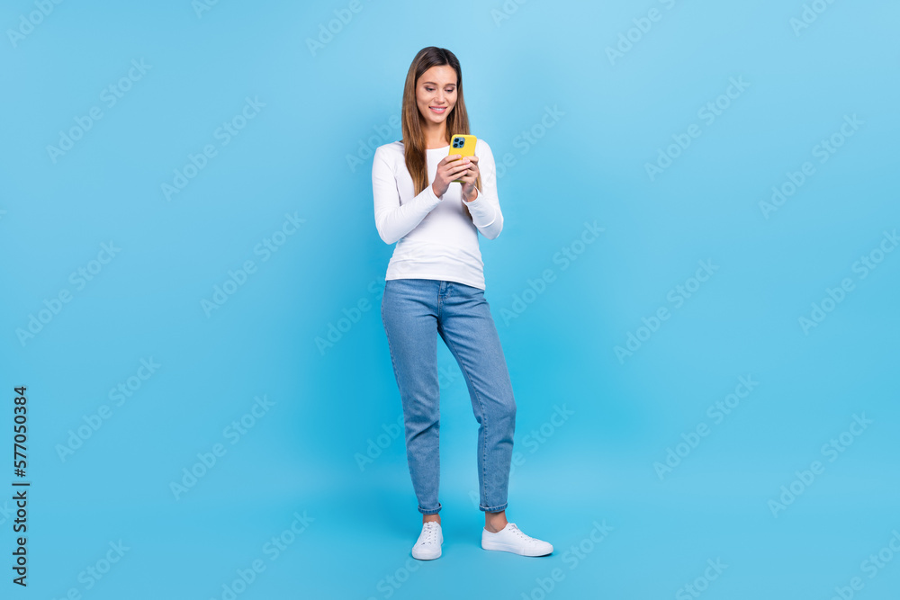 Full length photo of charming sweet lady dressed white shirt typing message modern device isolated blue color background Full length photo of charming sweet lady dressed white shirt typing message modern device isolated blue color background