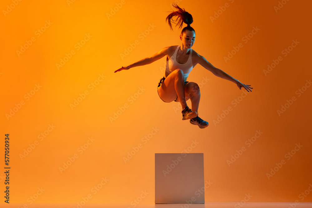 Workout. Young sportive girl, athlete training, jumping over block
