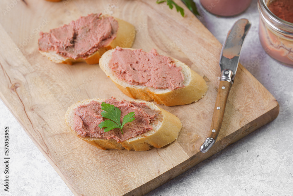 Homemade chicken liver pate on fresh french white wheat baguette slices on wooden plate, glass mason jars with cooked liverwurst, top view Homemade chicken liver pate on fresh french white wheat baguette slices on wooden plate, glass mason jars with cooked liverwurst, top view
