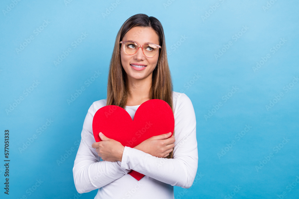 Photo of positive funny lady dressed white shirt spectacles cuddling red heart looking emtpy space isolated blue color background Photo of positive funny lady dressed white shirt spectacles cuddling red heart looking emtpy space isolated blue color background
