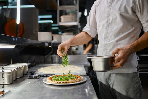 Chef sprinkling fresh greenery over traditionally made pizza