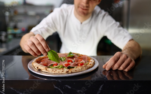 Chef pizzaiolo decorating pizza with fresh oregano leaves