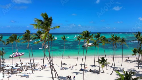 Aerial flight between palm trees above the public Bavaro beach with white sand. Turquoise water of the Caribbean sea and tourist yachts and boats. Punta Cana, Dominican republic photo