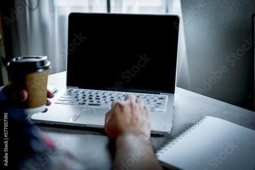 Man drinking hot americano while working on a laptop at home or cafe. Empty screen laptop.